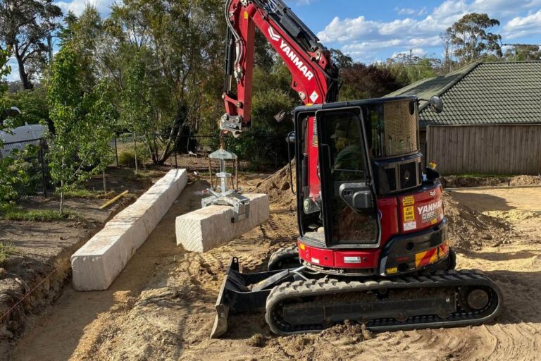 Excavator placing sandstone blocks for a retaining wall