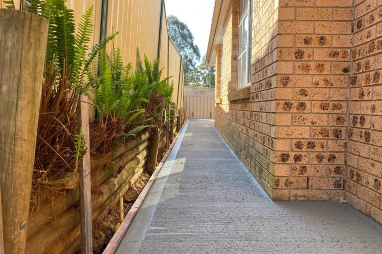 New concrete side path between a brick house and a timber fence